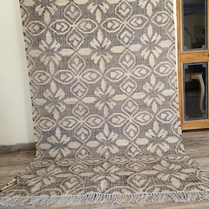 May include: A brown and cream patterned rug with a fringe border. The rug has a geometric design with a repeating pattern of stylized flowers.