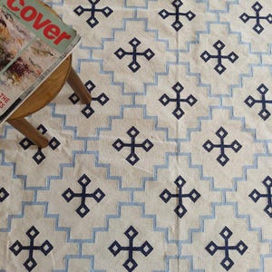 May include: A white and blue patterned rug with a geometric design. The rug features a repeating pattern of blue crosses on a white background. The rug is made of a soft, woven material.