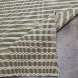 May include: A green and white striped rug with a woven texture. The rug is folded in half, showing the underside.