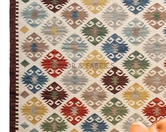 May include: A white rug with a geometric pattern in shades of red, blue, green, brown, and yellow. The rug has a fringe border.
