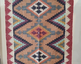 May include: A brown, black, red, green, and blue geometric patterned rug with a fringe border.