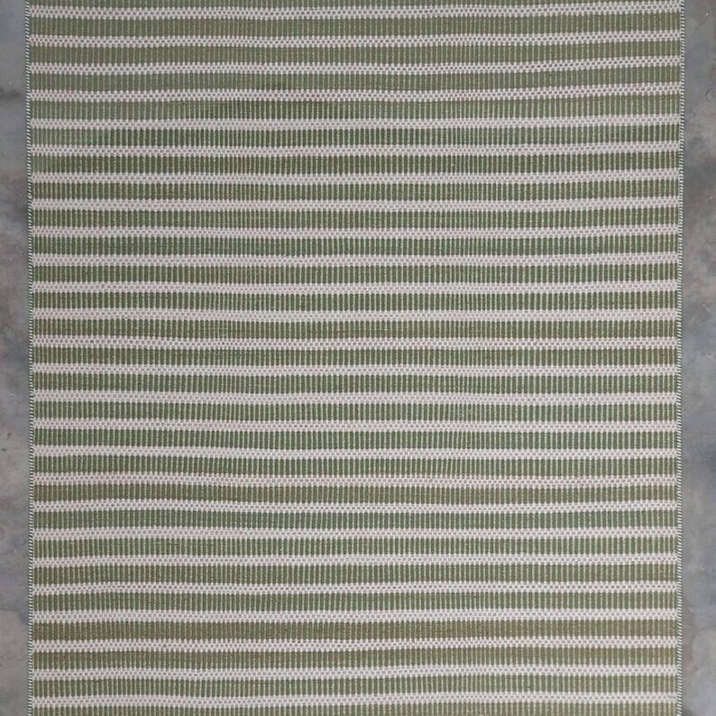 May include: A green and white striped woven rug with a subtle texture. The rug has a rectangular shape and is made of natural fibers.