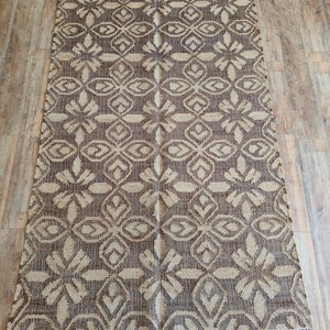May include: A brown and beige patterned rug with a fringe border. The rug has a geometric design with a repeating pattern of diamonds and flowers.
