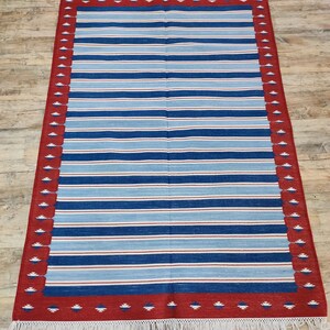 May include: A striped rug with a red and white border. The rug has a fringe on all sides.