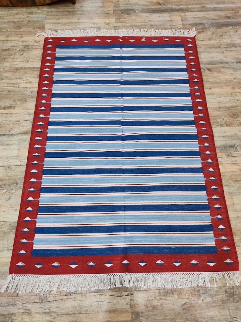 May include: A striped rug with a red and white border. The rug has a fringe on all sides.