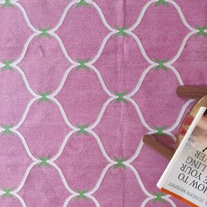 May include: Pink woven rug with a white and green geometric pattern. The rug has a subtle texture and a soft, muted color.