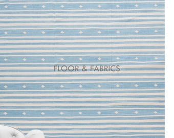 May include: A light blue and white striped rug with a subtle diamond pattern. The rug has a fringe border and is shown with a white armchair.
