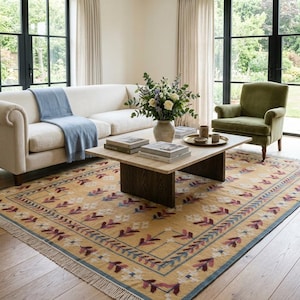 May include: A rectangular area rug featuring a mustard yellow base with a repeating pattern of stylized floral motifs in shades of burgundy, blue, and white, finished with a fringed edge and a thin blue border on a light-colored wooden floor.