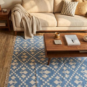 Puede incluir: Un sal&oacute;n acogedor con una alfombra azul y crema con estampado geom&eacute;trico y flecos. Una mesa de centro de madera con un libro y una taza. Un sof&aacute; beige con cojines y una manta completan la escena. El texto en la parte superior dice "Cozy Living Room Ideas".
