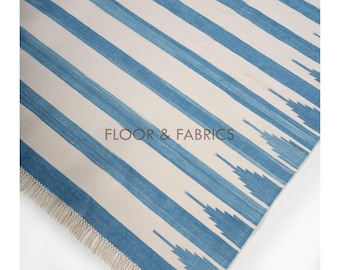 May include: A blue and white striped rug with a fringe border. The rug has a subtle ikat pattern in the blue stripes. "FLOOR & FABRICS" is printed in the center of the rug.