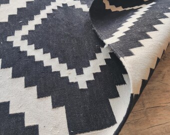 Puede incluir: Alfombra geométrica de patrón blanco y negro con fondo blanco y diseño en zigzag negro. La alfombra está doblada por la mitad y el borde es visible.