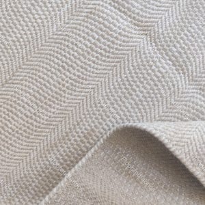 May include: Close-up of a beige and off-white chevron patterned rug. The rug's texture is visible, with a folded corner revealing the underside. The design features a repeating zigzag pattern, suitable for home decor.