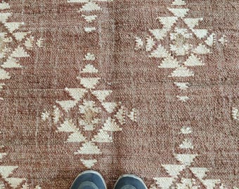 May include: A pair of dark blue sneakers with white laces on a brown and white patterned rug.