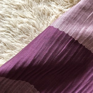 May include: A purple and pink fabric with a textured pattern. The fabric is folded in half and the pink side is on top.