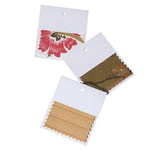 May include: Three fabric swatches on white card stock with a hole punched in the top corner. The swatches are a red floral print, a green and brown patterned fabric, and a tan fabric with a ribbed texture.