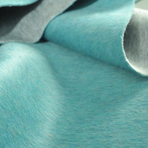 Puede incluir: Una tela suave de color azul turquesa con una textura sutil. La tela está doblada y drapeada, mostrando su tacto suave y lujoso.