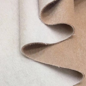 Peut inclure: Deux morceaux de tissu, un blanc et un beige, sont pliés ensemble. Le tissu est doux et duveteux.