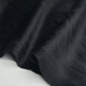 Può includere: Tessuto in pelliccia sintetica nera con una texture morbida e soffice. Il tessuto è liscio e ha una leggera lucentezza.