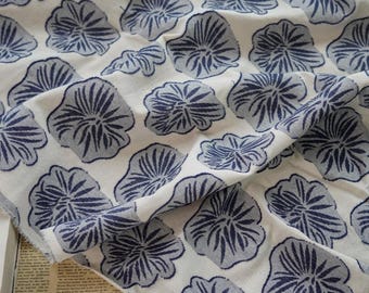 May include: White fabric with a repeating pattern of blue stylized floral designs. The fabric is folded and draped.