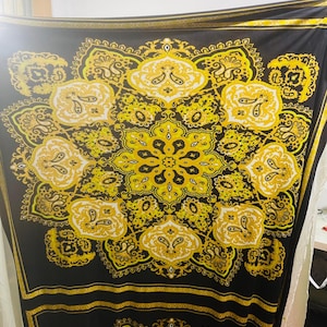 Może przedstawiać: Czarny materiał z dużym wzorem paisley w kolorze złotym i żółtym. Wzór jest powtarzalnym wzorem stylizowanych liści i kwiatów.