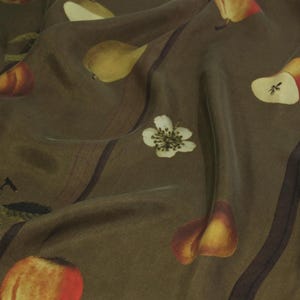 Puede incluir: Una tela verde con un patrón repetido de peras, manzanas y flores blancas. La tela tiene un brillo sutil y una textura suave y fluida.