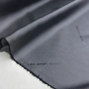 Puede incluir: Primer plano de una tela gris oscura con un brillo sutil. La tela tiene un borde sin terminar y las palabras "2018 MADE IN ITALY" están impresas en la superficie.