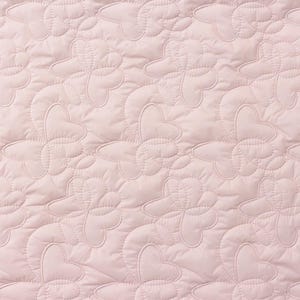 Può includere: Primo piano di un tessuto trapuntato rosa con un motivo ripetitivo di forme di fiori stilizzate.