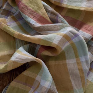 Könnte beinhalten: Nahaufnahme eines gefalteten Stoffes mit einem Karomuster. Der Stoff weist eine Mischung aus Farben auf, darunter Gelb, Braun, Rot und Blau. Das Karomuster besteht aus sich kreuzenden Linien, die ein gitterartiges Muster bilden.