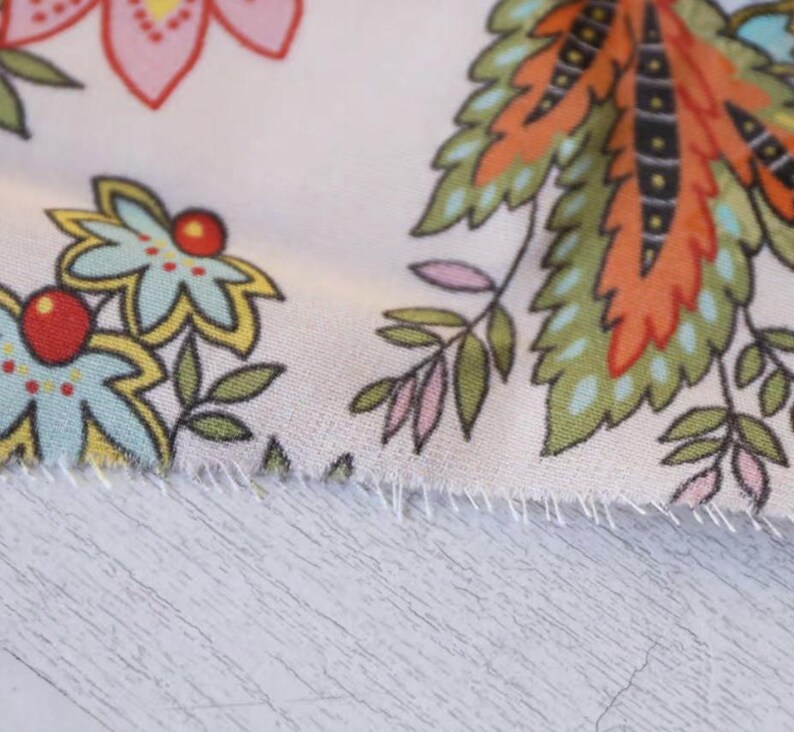 May include: Close-up of a floral fabric with a white background. The fabric features colorful flowers and leaves in shades of pink, blue, yellow, orange, and green. The edges of the fabric are frayed.