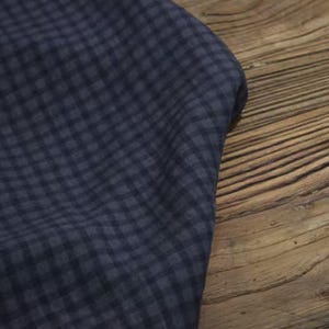 May include: A close-up of a navy blue fabric with a small checkered pattern. The fabric is draped over a wooden surface with visible grain. The fabric's texture and pattern are clearly visible.