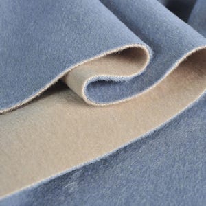 Puede incluir: Primer plano de una tela azul con forro beige. La tela es suave y peluda, y el forro es liso.