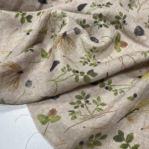 May include: Beige fabric with a botanical print featuring green leaves, brown seed heads, and black berries. The fabric has a natural, textured appearance, with a detailed illustration of forest elements. The design is repeated across the fabric.