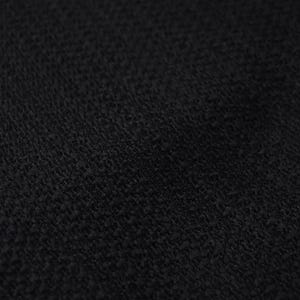May include: Close-up of a black fabric with a textured surface. The material appears to be woven, with a slightly irregular pattern. The dark color suggests a versatile textile suitable for various applications.
