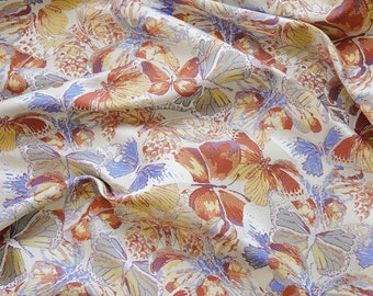 Könnte beinhalten: Ein weißer Stoff mit einem dichten, sich wiederholenden Muster aus Schmetterlingen in Rostorange, gedämpftem Gelb und Kornblumenblau. Das Textil weist eine sichtbare Webstruktur mit Falten auf, die Tiefe auf der Materialoberfläche erzeugen.