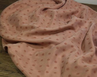 May include: A close-up of a soft, pink fabric with a subtle polka dot pattern. The fabric is draped and folded, showcasing its texture and drape.