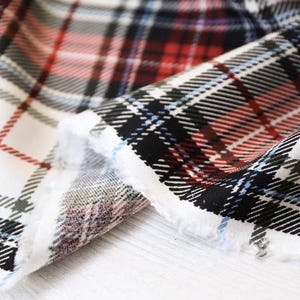 K&ouml;nnte beinhalten: Nahaufnahme eines Stoffes mit klassischem Karomuster. Der Stoff hat eine wei&szlig;e Basis mit sich kreuzenden Linien in Rot, Schwarz und Blau. Die Kanten des Stoffes sind ausgefranst und zeigen die Textur und die Schichten des Materials.