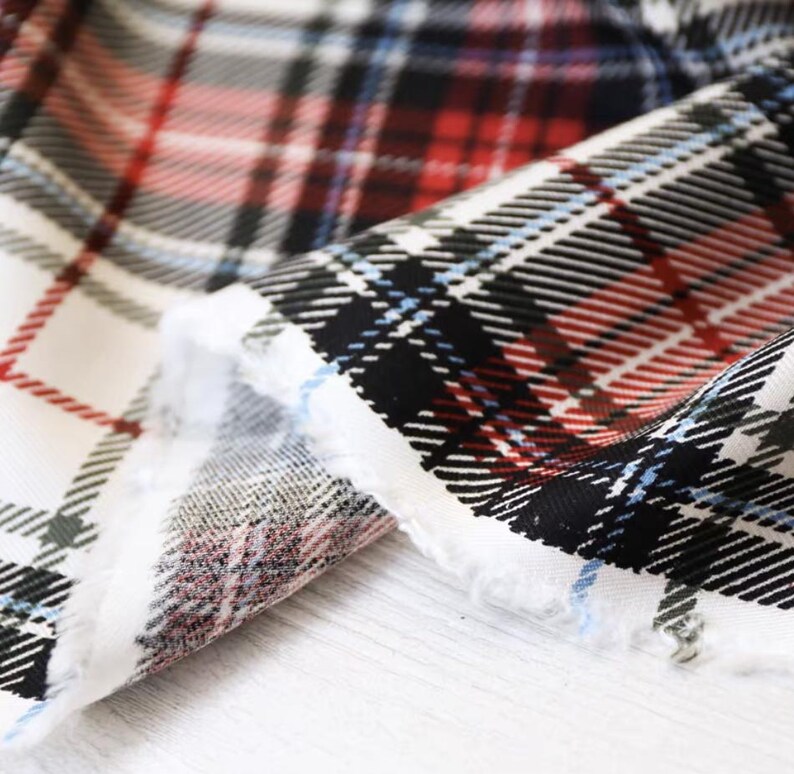 K&ouml;nnte beinhalten: Nahaufnahme eines Stoffes mit klassischem Karomuster. Der Stoff hat eine wei&szlig;e Basis mit sich kreuzenden Linien in Rot, Schwarz und Blau. Die Kanten des Stoffes sind ausgefranst und zeigen die Textur und die Schichten des Materials.