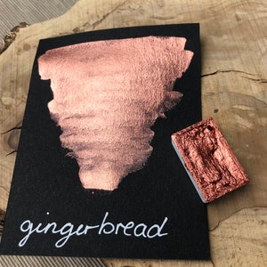 May include: A small square pan of metallic copper paint with a sample of the paint on a black card. The paint is labeled "gingerbread" in white script.