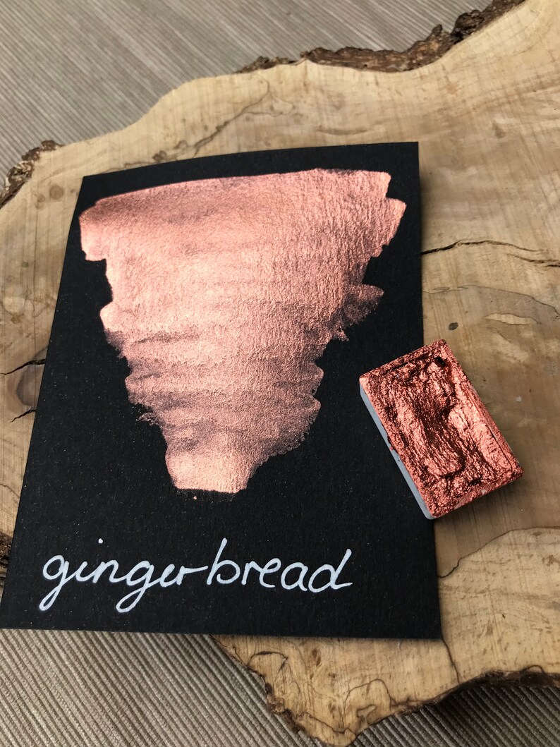 May include: A small square pan of metallic copper paint with a sample of the paint on a black card. The paint is labeled "gingerbread" in white script.