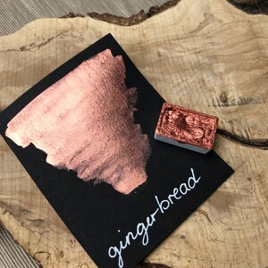 May include: A small sample of copper-colored ink on a black card with the word "gingerbread" written in white. The ink is metallic and shimmery.