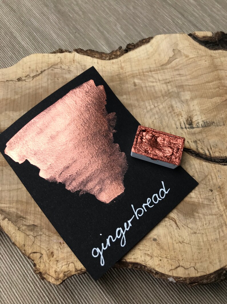 May include: A small sample of copper-colored ink on a black card with the word "gingerbread" written in white. The ink is metallic and shimmery.