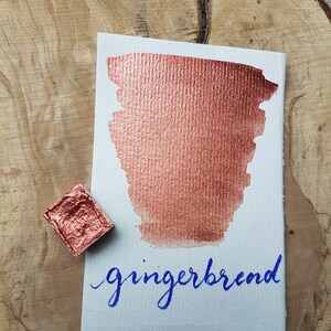May include: A small pan of metallic copper watercolor paint with a sample of the paint on a white card. The card has the word "gingerbread" written in blue ink.