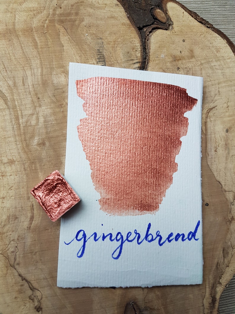 May include: A small pan of metallic copper watercolor paint with a sample of the paint on a white card. The card has the word "gingerbread" written in blue ink.