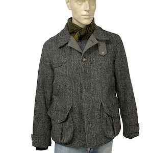 May include: A gray herringbone tweed jacket with large front pockets and a button closure. The jacket has a gray collar and is worn over a green and black patterned scarf. The mannequin is also wearing blue jeans.