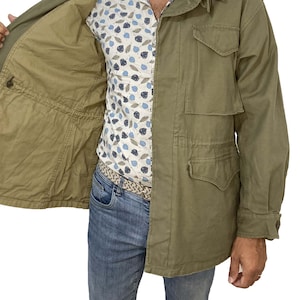 May include: A green field jacket with a zipper closure and multiple pockets. The jacket is unbuttoned and the lining is visible.