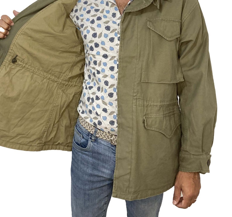 May include: A green field jacket with a zipper closure and multiple pockets. The jacket is unbuttoned and the lining is visible.
