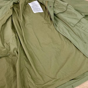 May include: A green military-style jacket with a zipper and a flap pocket. The jacket is unbuttoned and turned inside out, showing the lining.