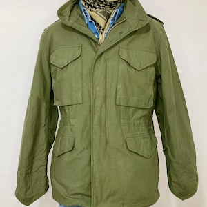 May include: A green military-style jacket with a zipper closure and multiple pockets. The jacket has a drawstring waist and a hood.