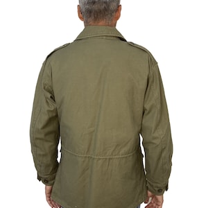 May include: A green utility jacket with a button-up front and flap pockets. The jacket has a drawstring waist and a relaxed fit.
