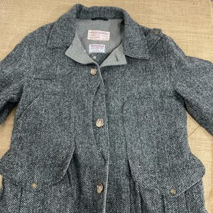 May include: A gray herringbone tweed jacket with a notched collar, button closures, and two front pockets. The jacket has a gray lining and a label that reads "Filson Garment".
